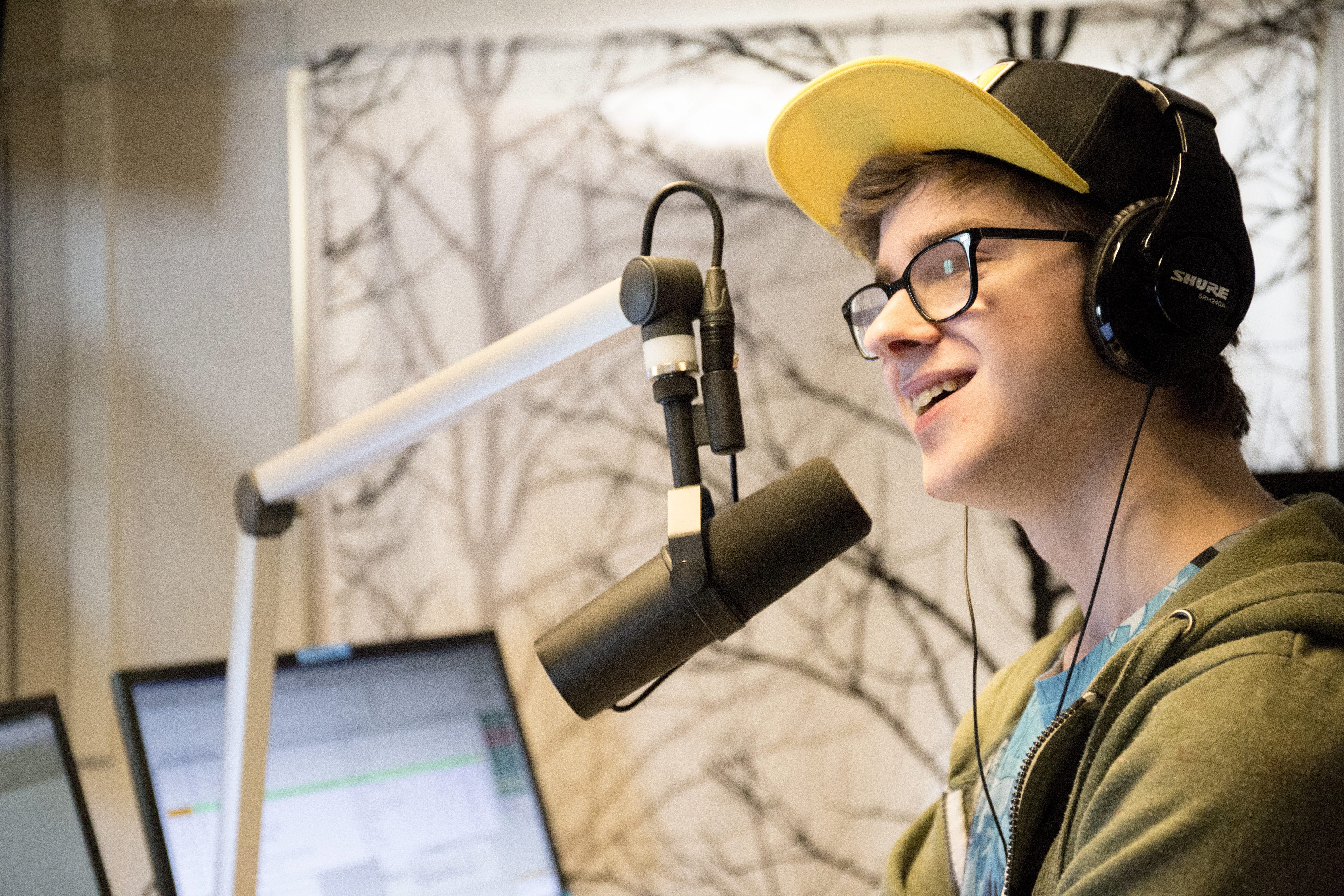 En kvinna med hörlurar och hatt framför en mikrofon.