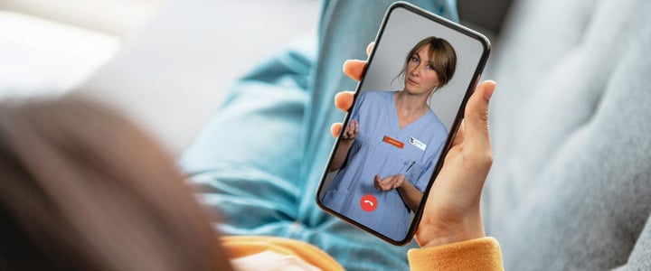 En kvinna som håller i en mobiltelefon med en bild av en sjuksköterska på skärmen.