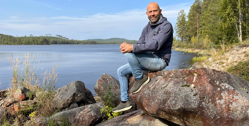 En man sitter på en sten intill ett vattendrag.