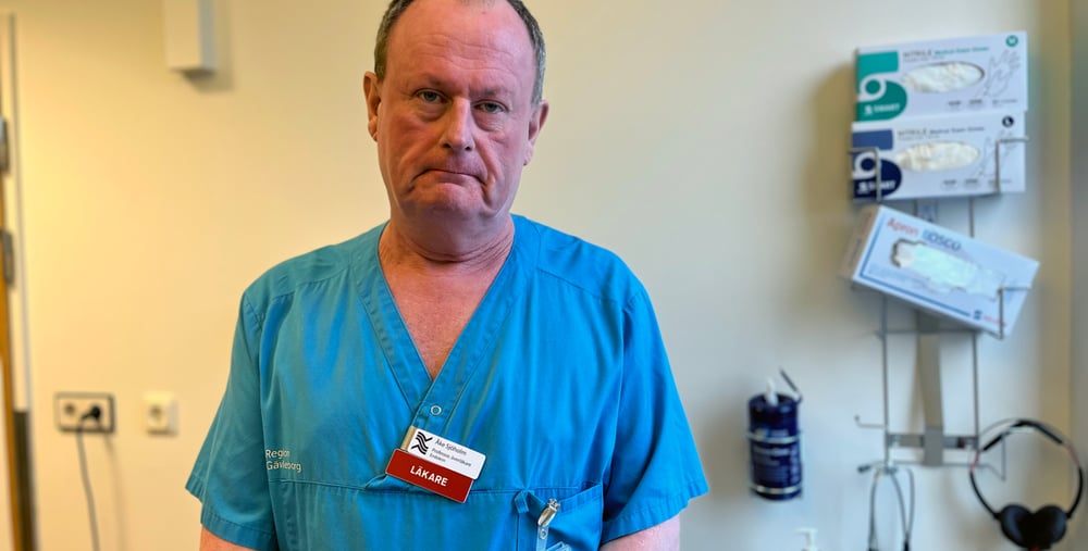 Man med blå skjorta vita byxor, står och ser i kameran, kort mörkt hår, medelålders