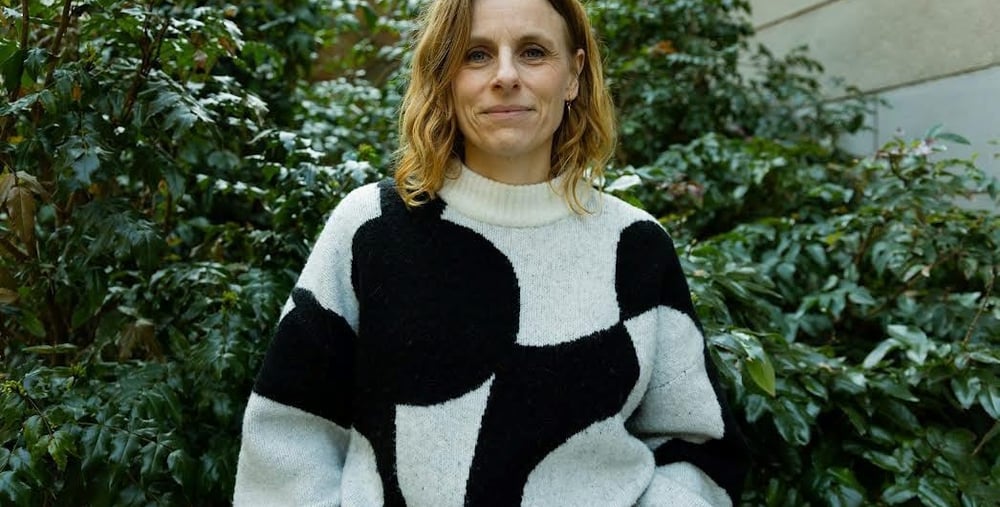 Person ståendes framför en grön buske iklädd en svart och vit mönstrad tröja.