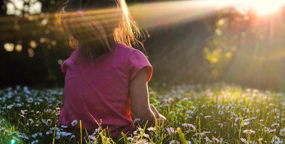 Flicka sittandes ute på gräsfält i solnedgång