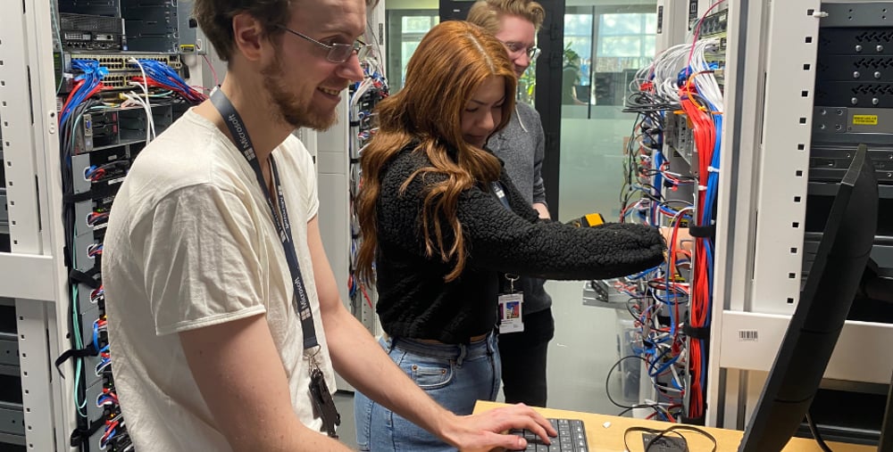 Tre personer arbetar vid servrar och kablage i en datahall.