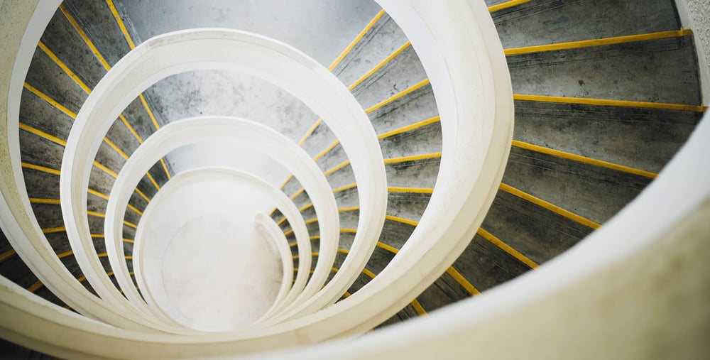 Spiralformad trappa med vita räcken och gula markeringar på trappstegen, sedd uppifrån.