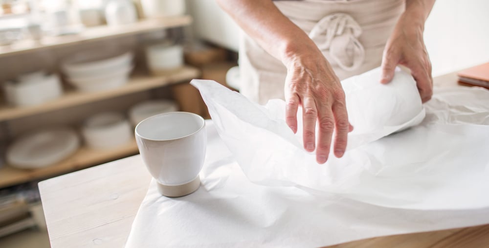 Närbild på ett par händer som slår in keramik.