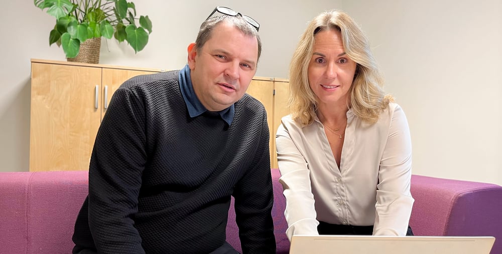 Sam Cole och Malin Schönning sitter i en vinröd soffa med en dator framför sig på ett bord. 