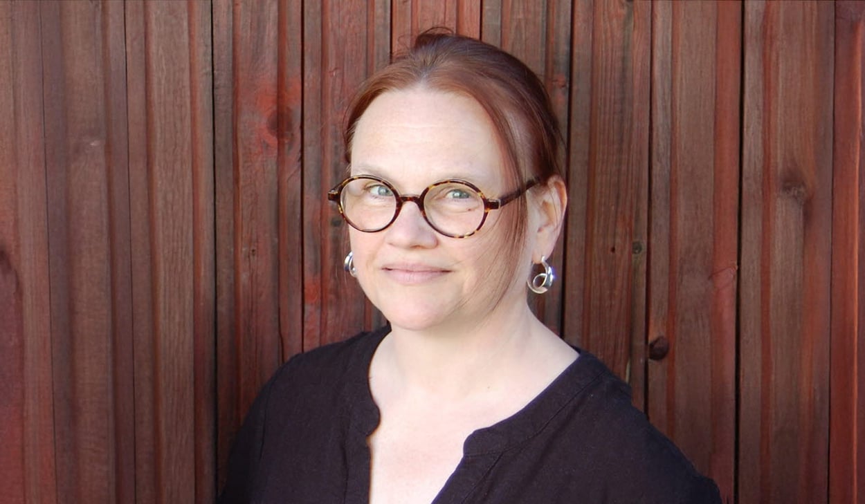 Porträtt av en person mot en träpanel i bakgrunden.