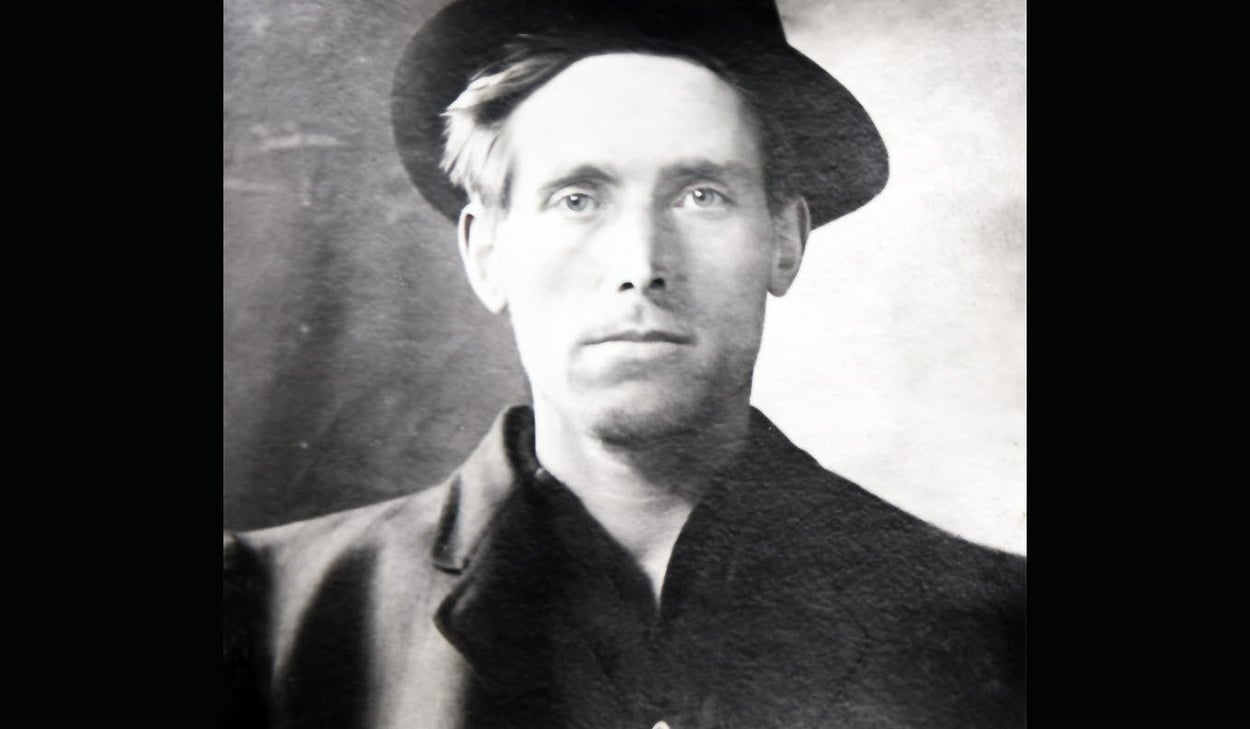 Svartvit bild av författare Joe Hill iklädd rock och hatt. 
